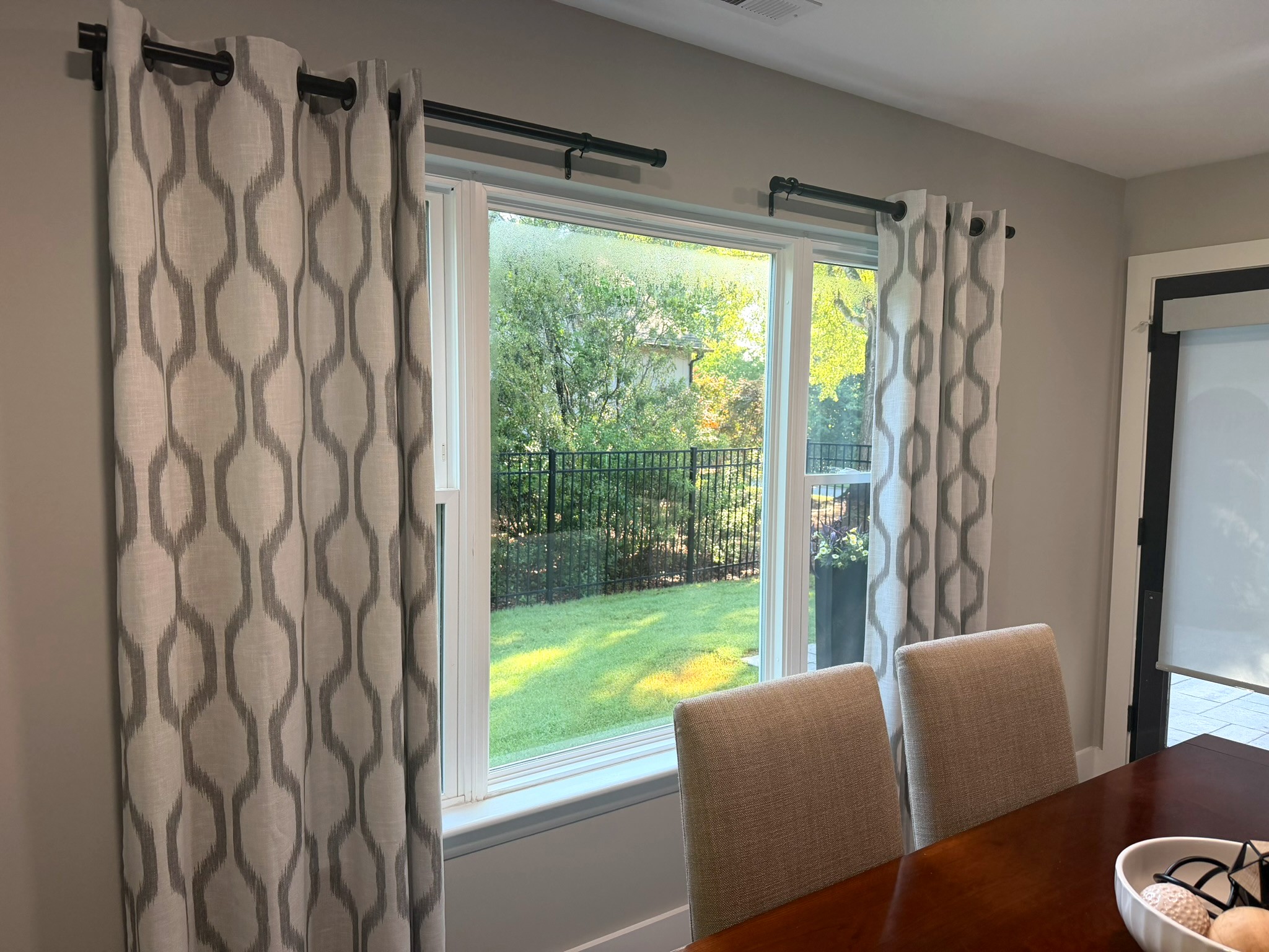 Dining room windows dressed in ikat-pattern grommet drapery on black iron rods, framing a green backyard view