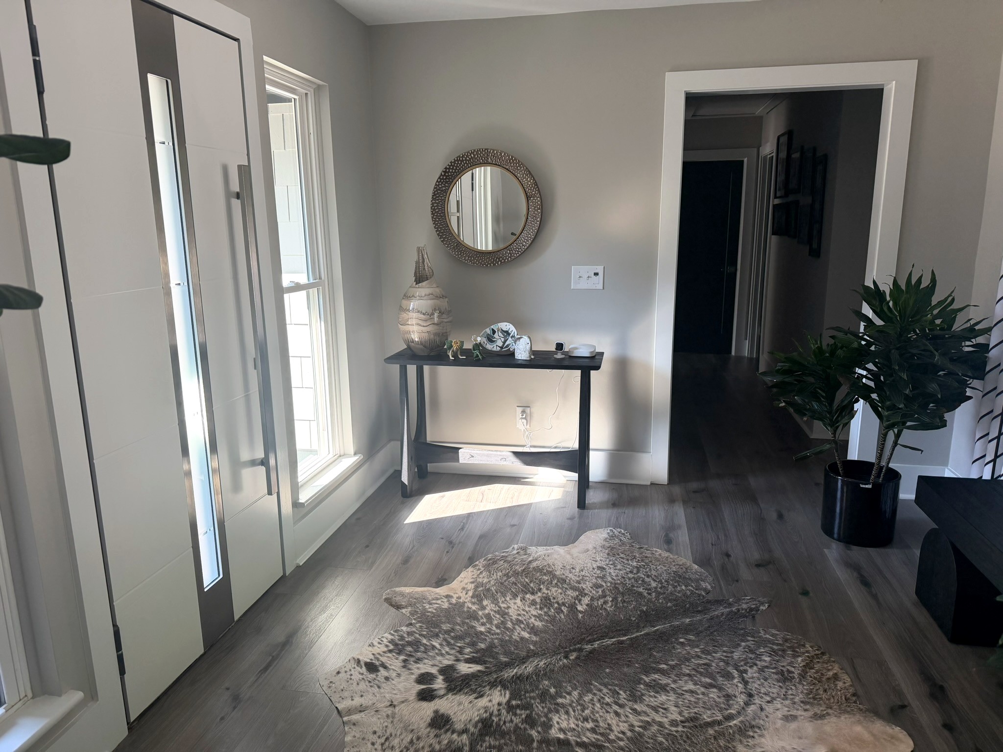 Warm, inviting foyer with a hammered-metal round mirror over a black console table and a cowhide rug on wide-plank floors