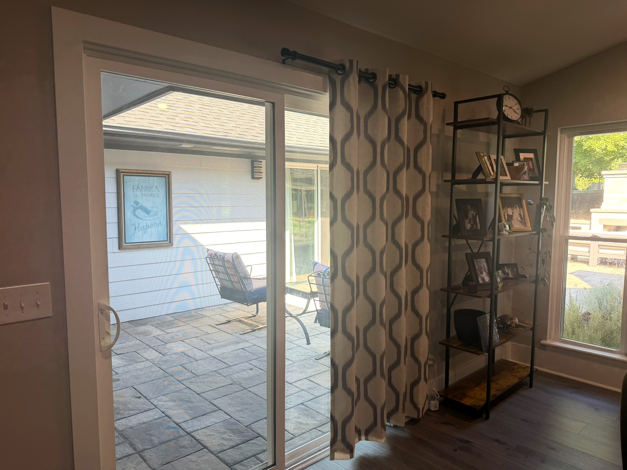 Sliding patio door with patterned drapery beside an iron ladder shelf of framed photos