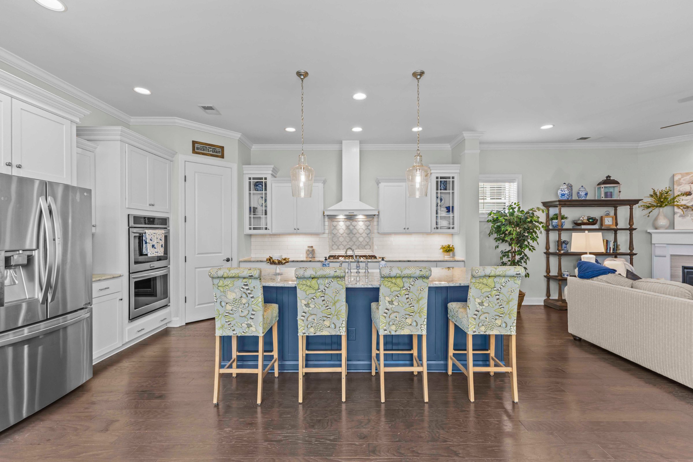 Sage-green kitchen with white cabinetry, a blue island, and floral counter stools — designed by Donna Marlowe