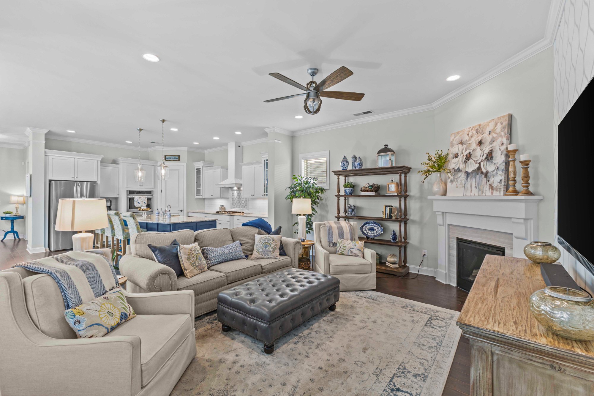 Open-concept living room and kitchen with neutral sofas, layered blue-and-white accents, and a fireplace