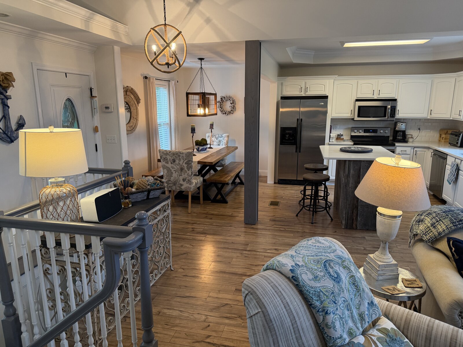 Entry after renovation — an open landing with a scrolled iron console, nautical accents, and a dining table framing the flow into the kitchen