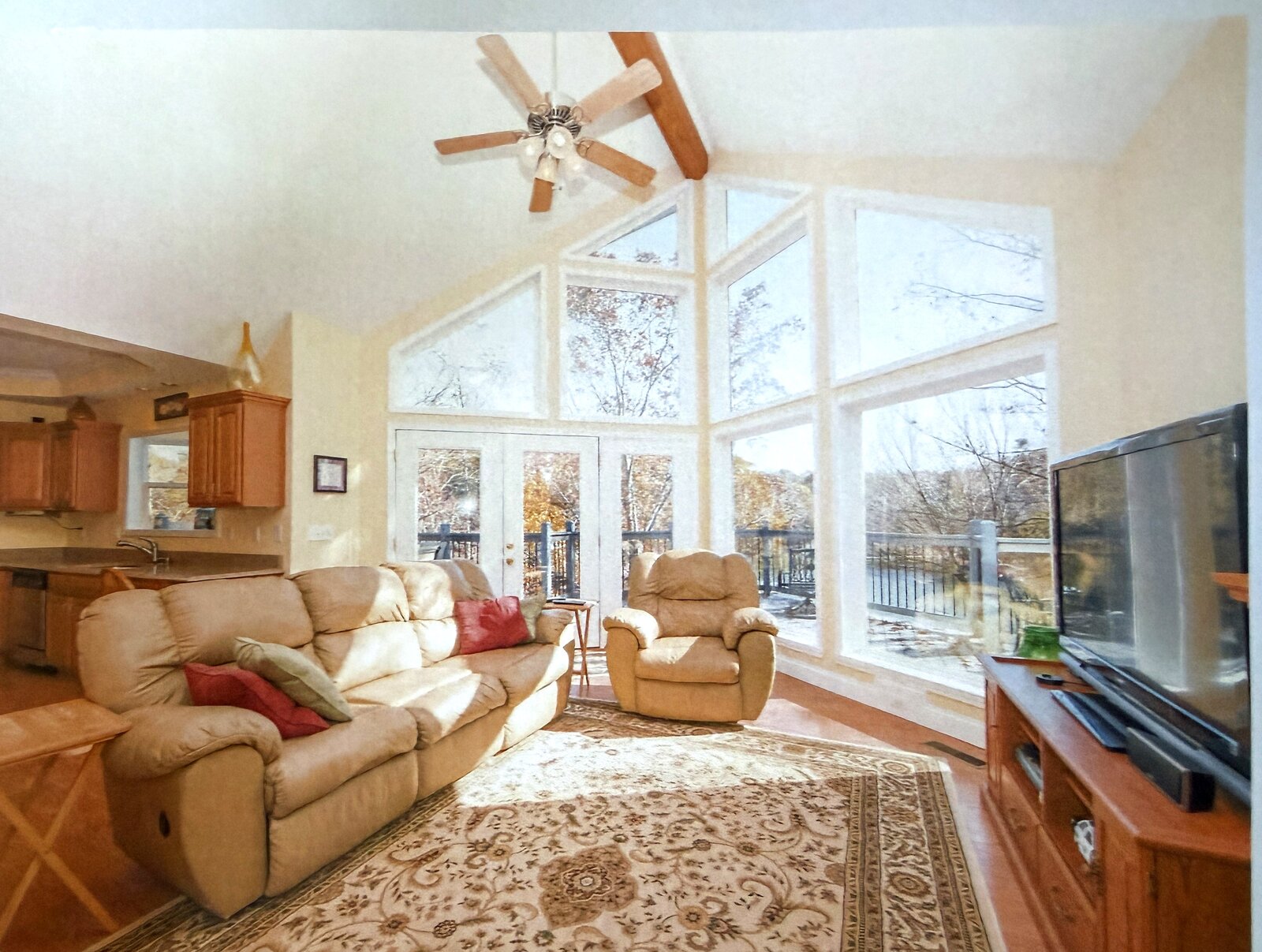 Great room before renovation — tall windows, a beige leather recliner set, oak media console, and a patterned area rug
