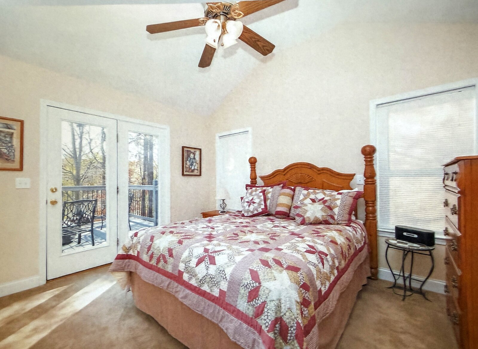Primary bedroom before renovation — an oak poster bed with a burgundy star quilt and dated wall art