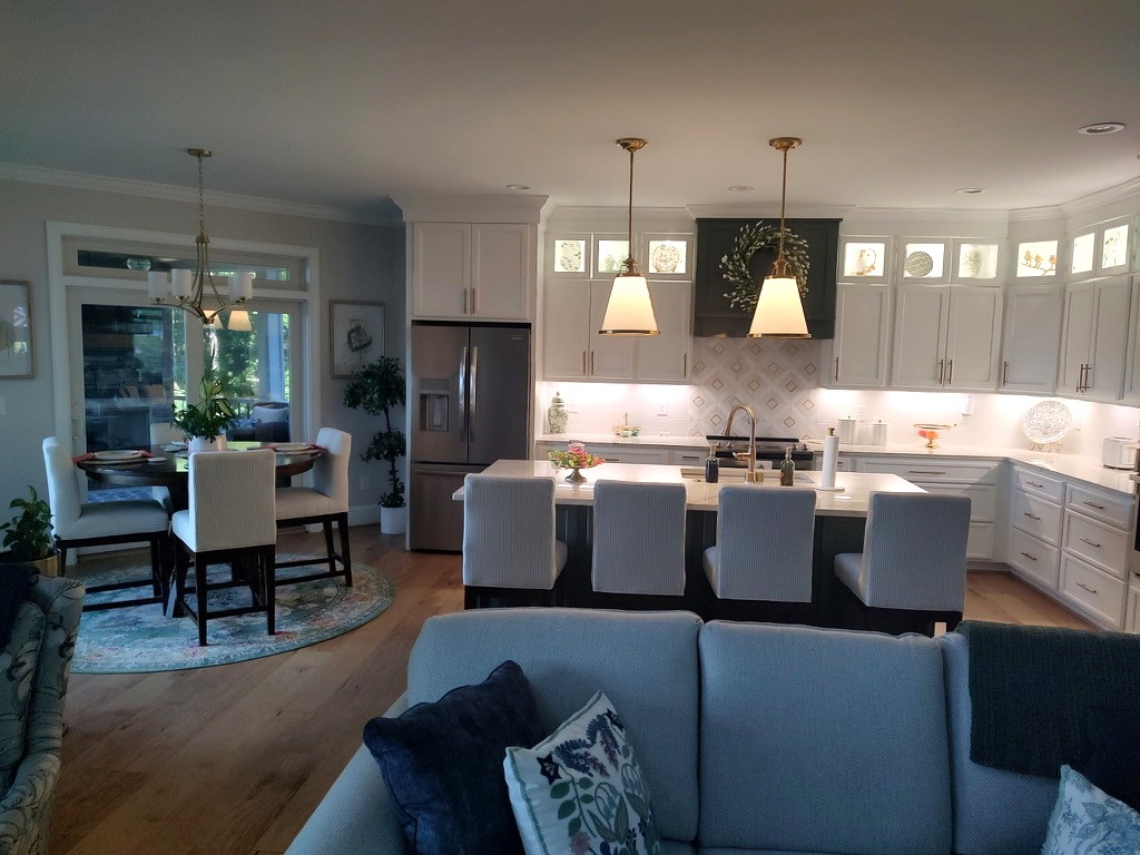 Open white kitchen with a dark hood, glass-front cabinets, and an island with striped upholstered stools