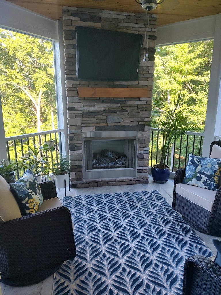 Screened porch with a stacked-stone fireplace, wicker seating, and a blue leaf-pattern rug