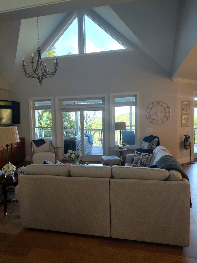 Vaulted great room with a triangular peak window, iron chandelier, and cream sofa framing the mountain view