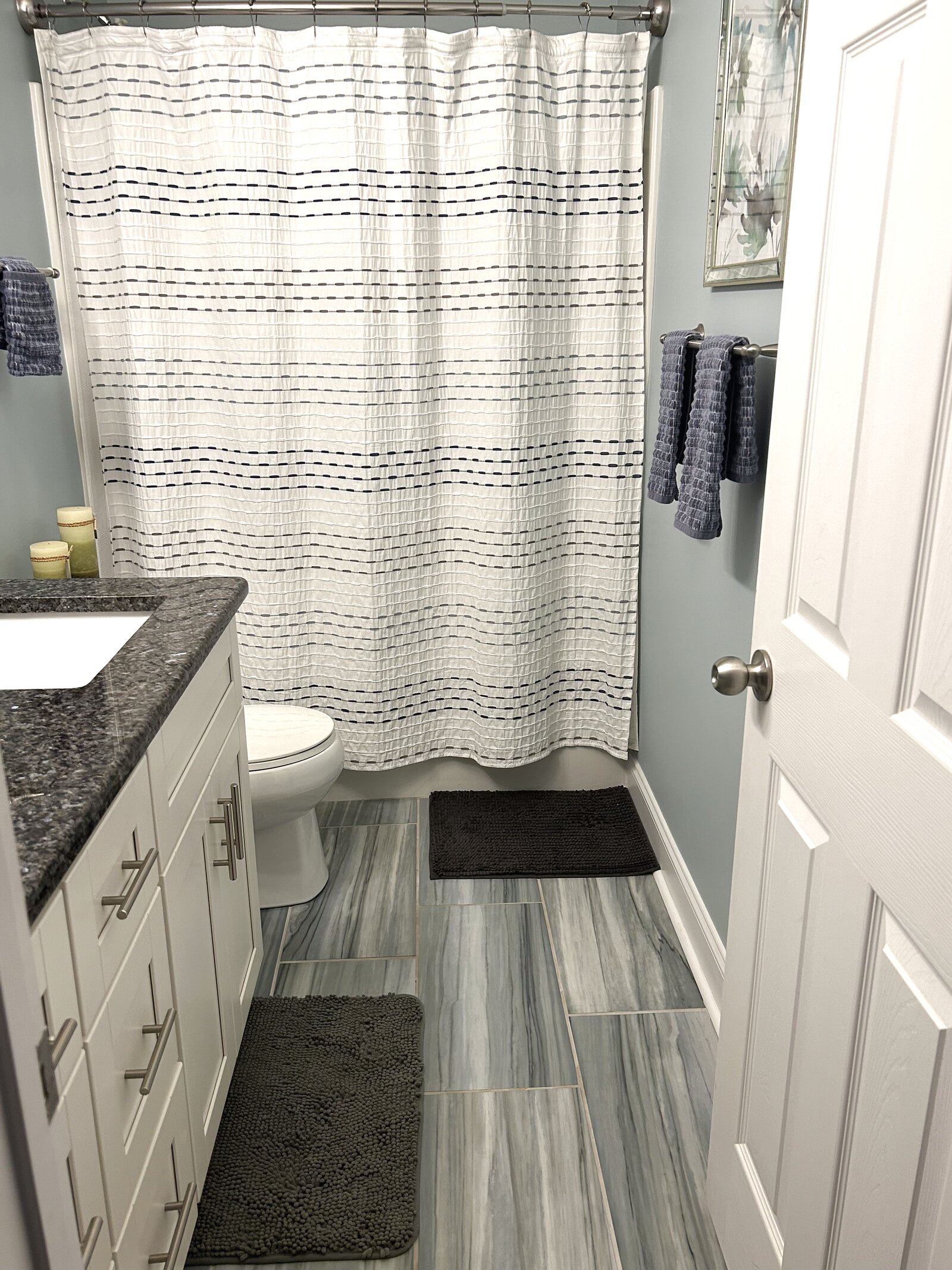 Bathroom with a stone-topped white vanity, striped curtain, marbled grey tile floor, and soft blue walls
