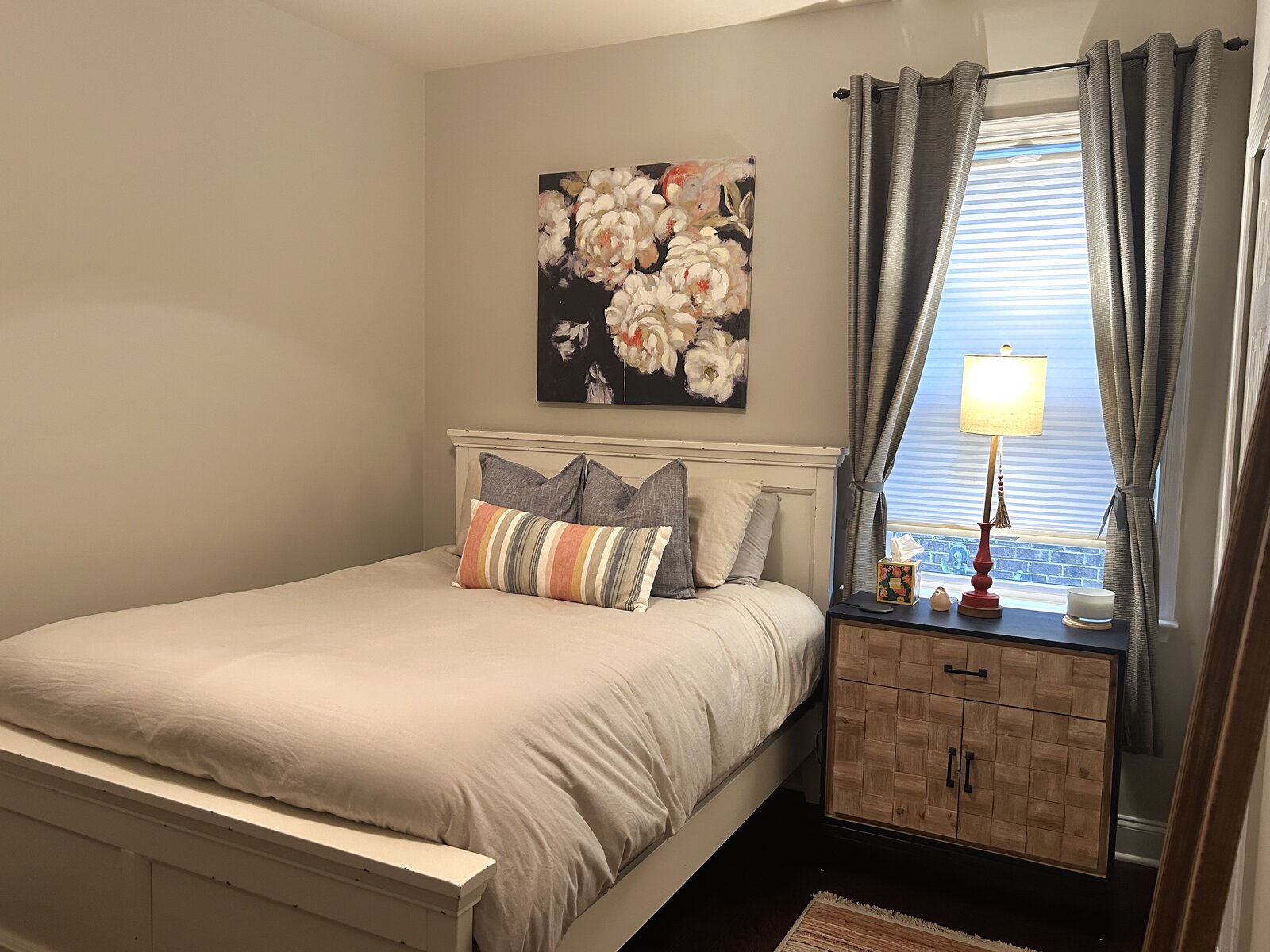 Guest bedroom with a floral canvas over a white bed, a woven-front nightstand, and a striped lumbar pillow