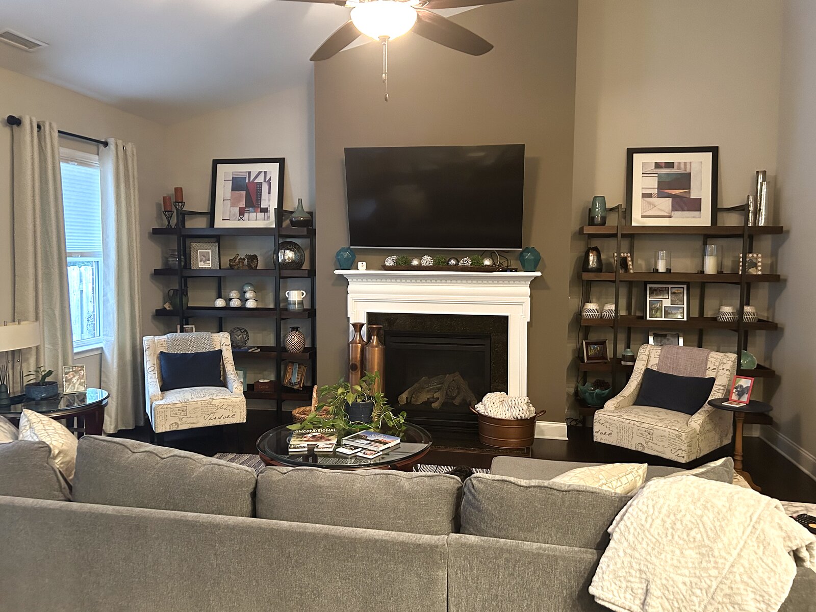 Living room with a fireplace framed by twin dark-wood shelving units styled with art and objects, a grey sectional, and script-print accent chairs