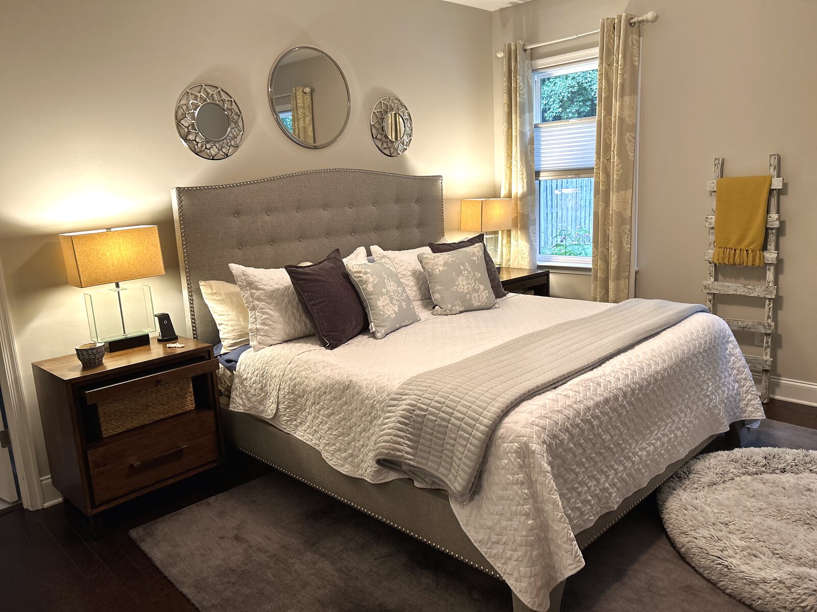 Primary bedroom with a tufted upholstered headboard, a trio of round mirrors, layered neutral bedding, and warm lamplight