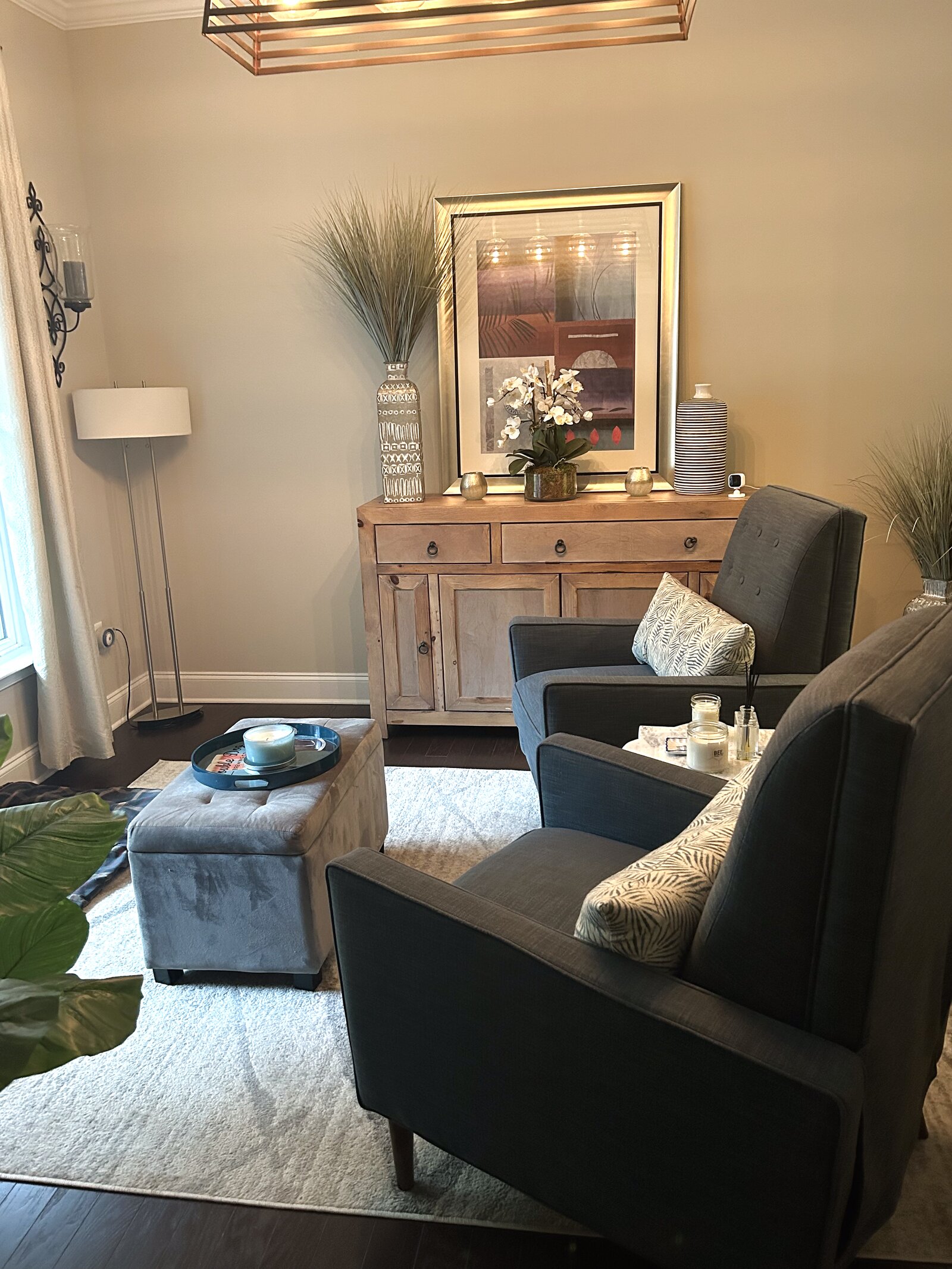 Sitting room with charcoal accent chairs, a reclaimed-wood console, framed abstract art, and a linen ottoman on a soft area rug