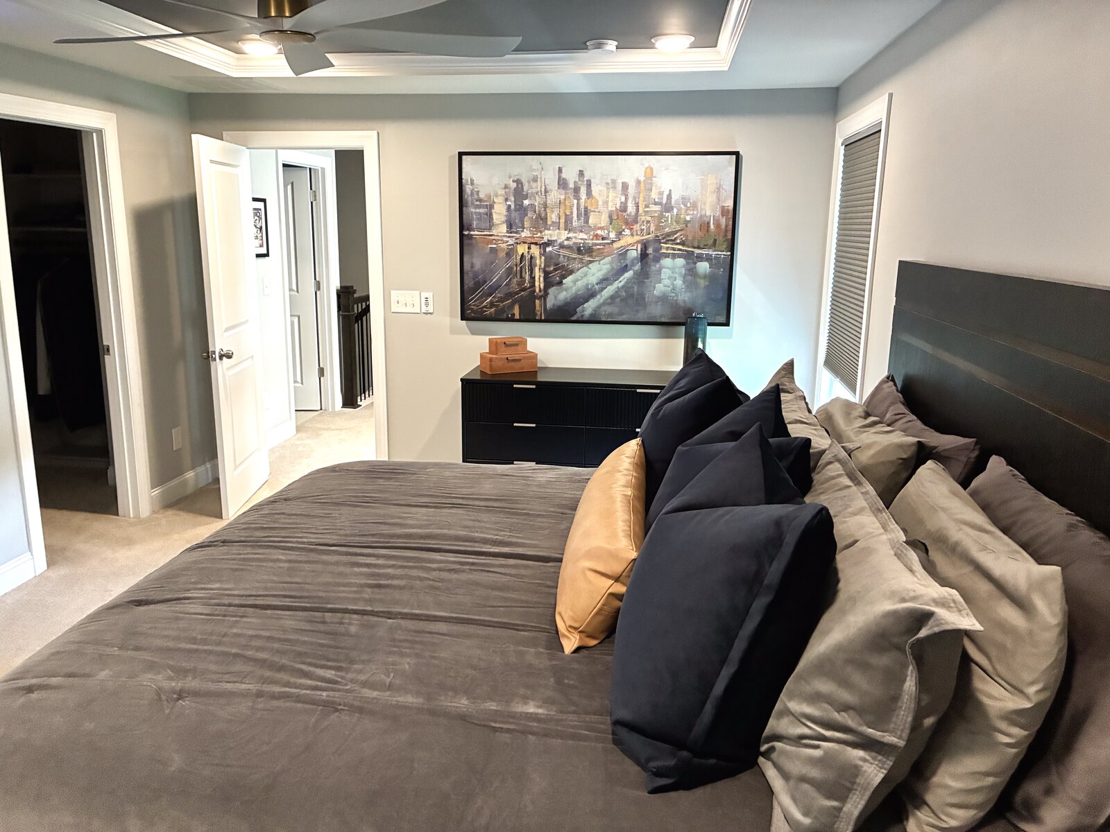 Primary bedroom — framed city-skyline canvas over a black dresser, styled with warm brass and camel-leather accents